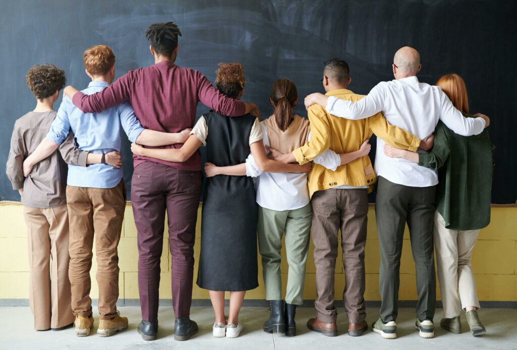 pexels-photo-3184396-3184396 A diverse group of adults in casual outfits hugging in front of a chalkboard, symbolizing teamwork.